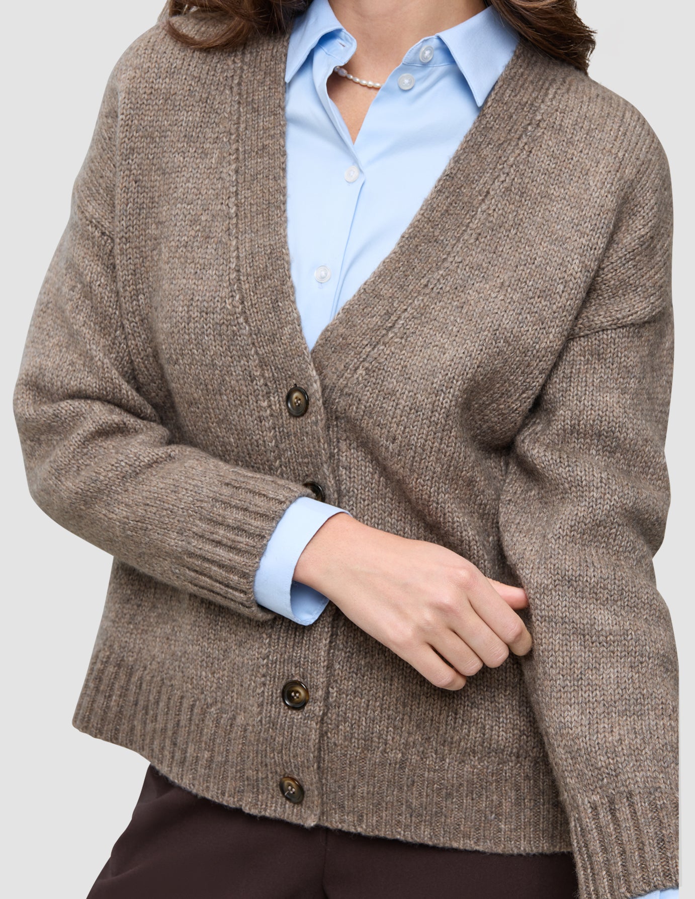 En kvinde har en tyk, blød uldstrikket cardigan i farven taupe-melange på over en lyseblå skjorte med krave.